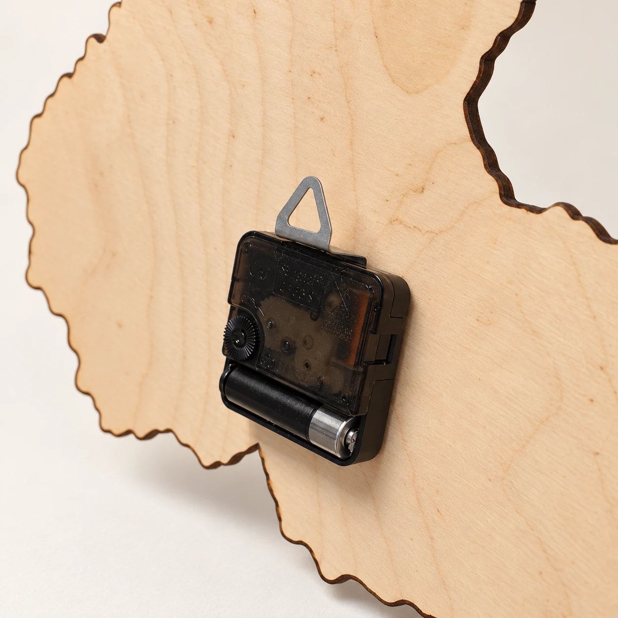 Rückseite der Holz-Wanduhr mit schwarzem Uhrwerk und dreieckiger Aufhängeöse aus Metall.
